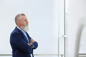 Wall Mural - Portrait of handsome mature man in elegant suit looking out window indoors