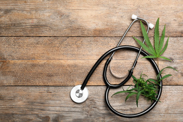 Wall Mural - Hemp leaves and stethoscope on wooden background, flat lay. Space for text