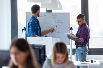 business young man pointing on whiteboard while discussing with his colleague of they new project in