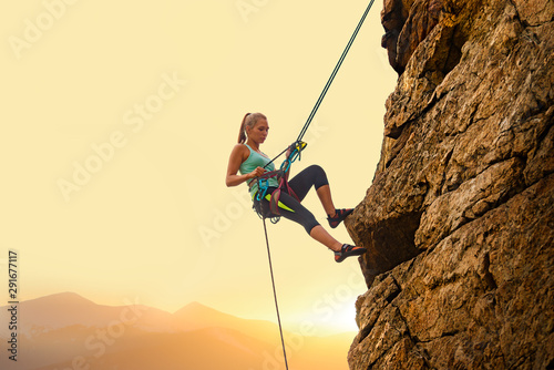 Fotomural Beautiful Woman Climbing on the Rock at Foggy Sunset in the Mountains