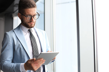 Wall Mural - Modern business man in formalwear using digital tablet while standing near window in the office