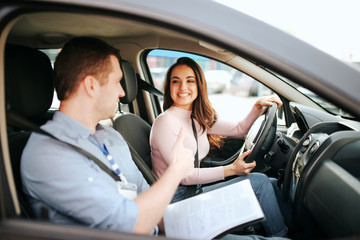 Male auto instructor takes exam in young woman. Practical issue. Cheerful happy and positive student look at teacher and smile.