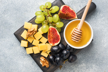 Wall Mural - Cheese cubes, fresh fruit figs grapes Honey walnut on wooden chopping Board. Copy space.