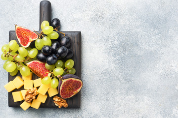 Wall Mural - Cheese cubes, fresh fruit figs grapes Honey walnut on wooden chopping Board. Copy space.