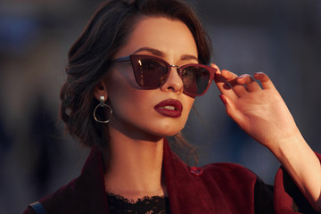 Wall Mural - Closeup portrait of young elegant woman wearing sunglasses. Pretty girl with hairstyle and makeup. Outdoor portrait. Sunset light.