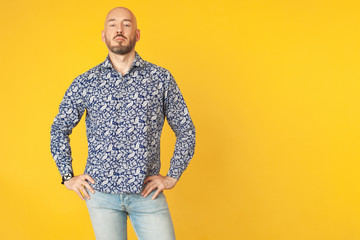 Fabulous at any age. Portrait of 40-year-old vegan man standing over light yellow background in blue shirt, jeans. Good figure. Hipster style. Bald shaved head. Copy-space. Studio shot