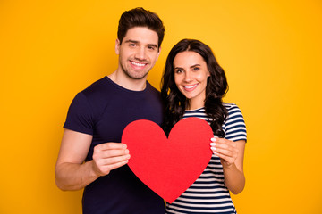 Poster - Photo of cheerful nice couple toothily smiling holding big red heart in love with each other while isolated with yellow background