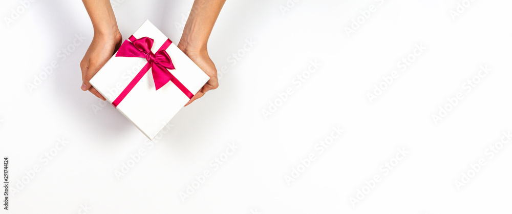 Child hands holding present gift box tied with ribbon on white background. Top view, place for text. Holiday concept - obrazy, fototapety, plakaty 