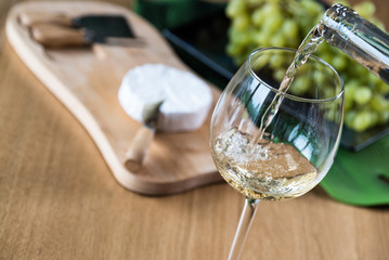 Wall Mural - Pouring white wine into the glass against wooden background