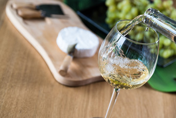 Wall Mural - Pouring white wine into the glass against wooden background