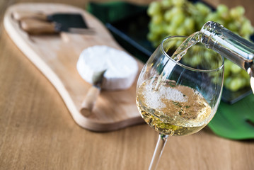 Wall Mural - Pouring white wine into the glass against wooden background