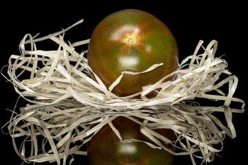 One whole fresh green red tomato in nest isolated on black glass