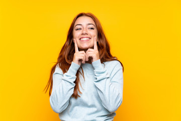 Wall Mural - Teenager redhead girl over isolated yellow background smiling with a happy and pleasant expression