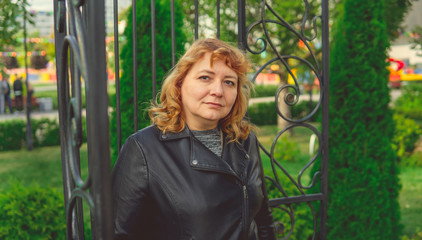 Woman against fence in garden. Content woman looking dreamily away while standing in green park against ornamental iron fence