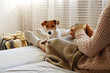 © Evrymmnt - Young woman and her adorable jack russell terrier puppy sitting on couch cozied up, covered with blanket. Lazy afternoon at home with loved pet concept. Close up, copy space, interior background.