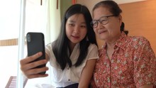 Asian Grandmother And Her Niece Having Fun With Using Smartphone And Taking Selfie Together, Family Concept