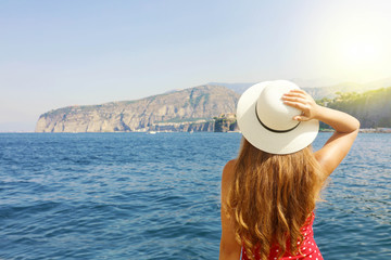 Wall Mural - Summer holiday in Italy. Back view of young woman holding her hat with Sorrento Peninsula on the background, Sorrento Coast, Italy.