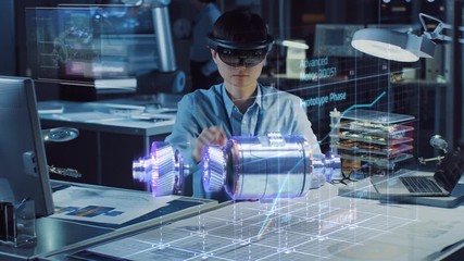 Fototapete - Industrial Factory Chief Engineer Wearing AR Headset Designs a Prototype of an Electric Motor on the Holographic Projection Blueprint. Futuristic Virtual Design of Mixed Technology Application.