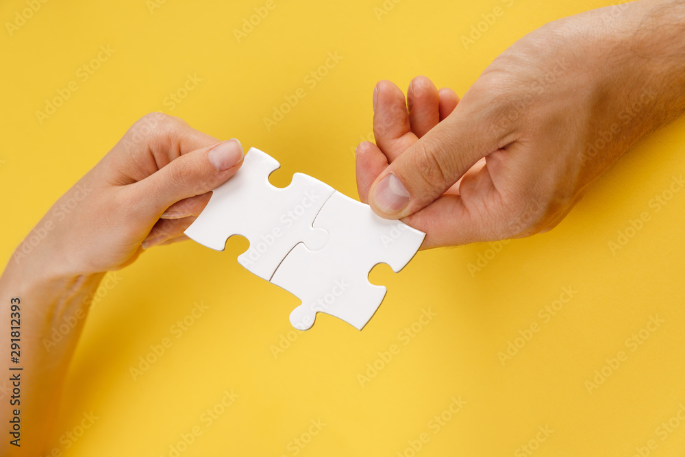 cropped view of man and woman matching pieces of white puzzle on yellow background - obrazy, fototapety, plakaty 