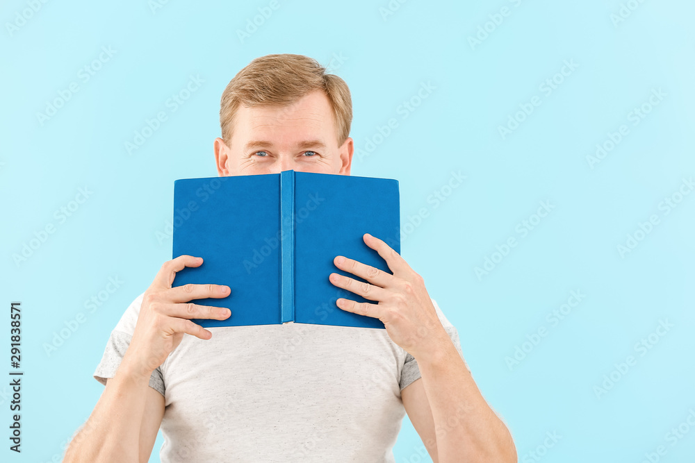 Portrait of handsome man with book on color background