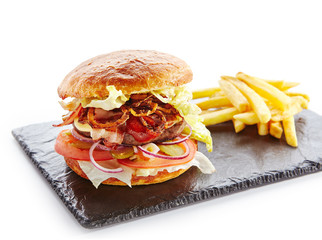 Canvas Print - Fresh Beef Burger with Bacon, Fried Onions, Tomato Sauce, Pickled Cucumbers, Green Lettuce, Cheese and French Fries Garnish. Hamburger or Beefburger on Natural Black Stone Plate Isolated on White