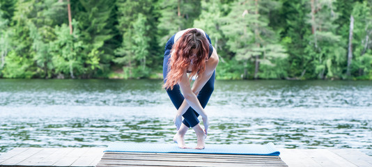 Wall Mural - Young girl practicing yoga in the nature on the lake. Female happiness. Concept of healthy life and natural balance. Landscape background, space for text