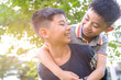 Joyful older brother giving younger brother a piggyback while playing and laughing with expressions, having fun.Asian smiling boy playing in garden and nature background.