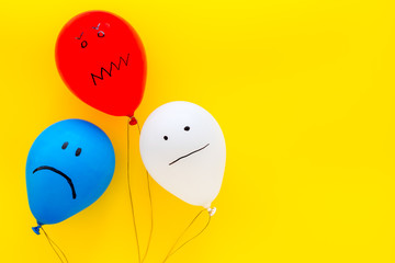 Wall Mural - Negative emotions concept. Balloons with drawn faces on yellow background top view space for text