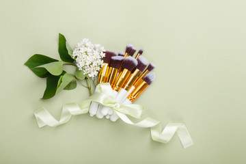 Wall Mural - Set of brushes for make up on green background with lilac white bloom. Women's secrets. Tools for make up artist with decorative cosmetics. Spring mood