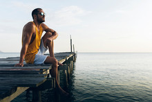 Young Man Sitting On Pier Near Sea
