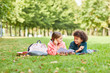 © AnnaStills - Two school children lying together on green grass with books and talking to each other during reading