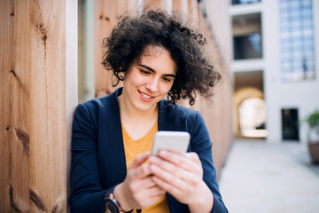 Wall Mural - A happy young business woman with smartphone standing outdoors.