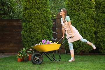 Happy young woman with wheelbarrow working in garden