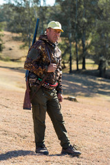 Wall Mural - Hunting period, autumn season open. A hunter with a gun in his hands in hunting clothes in the autumn forest in search of a trophy. A man stands with weapons and hunting dogs tracking down the game.	