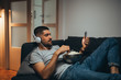 men listening music on headphones and using his smartphone, relaxed on sofa at his home