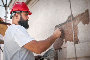 Male worker plastering old building wall using cement plaster mix