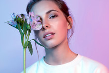 Beautiful Woman In White T-shirt Covering Face With Wonderful Blossom In Neon Light. Portrait Of Lovely Female Looking At Camera With Tenderness. Beauty And Fashion Concept