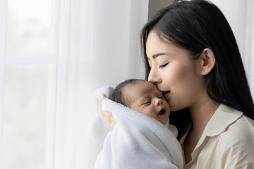 portrait of asian young mother kissing her cute newborn baby in white bed room. wife and mother's da