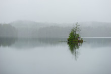 Small Shed On Minute Green Island With Small Trees In Lake On Foggy Day
