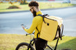 © rh2010 - Young courier delivering food on a bicycle, checking order with a smart phone while standing on the street in the city. Delivery service concept