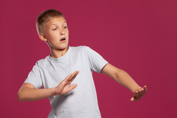 Close-up portrait of a blonde teenage boy in a white t-shirt posing against a pink studio background. Concept of sincere emotions.