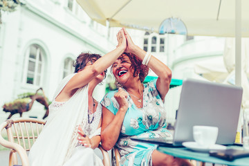 Two senior female friends are giving high five, celebrating success while looking each other