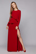 Full shot of young blonde European lady with long straight hair wearing a stylish red maxi dress decorated with an asymmetric frill, a basque and a side midthigh hem tear. 