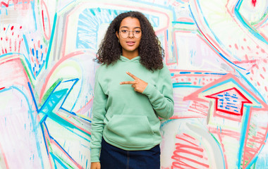 young pretty african american woman feeling happy, positive and successful, with hand making v shape over chest, showing victory or peace against graffiti wall