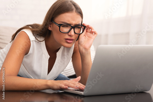 Fotomural Woman Looking Through Eyeglasses At Laptop Sitting On Couch Indoor