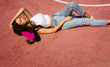 © NASTYA PALEHINA - young sports happy sexy brunette girl with long hair in jeans and white top is laying fashion under the sun on pink mini skateboard with hand near head on the red sports court background, free space