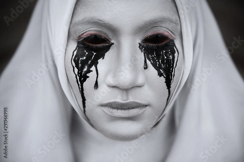 Fotografía A gloomy portrait of a ghostly pale nun in white robes with black eye sockets and black smudges under them