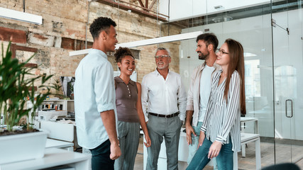 Wall Mural - Happy and successful. Group of cheerful business people standing in the modern office, smiling and discussing something