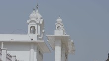 A Steady Closeup Shot Of The Bell Tower Of A Tall Indian Building Structure Showing Its Facade Painted In White And Its Bulbous Dome With Decorative Spires..