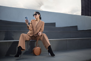 Wall Mural - Portrait of a successful business woman sitting on stairs. the phone is in her hands. City background